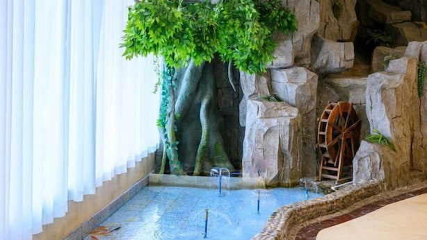 Ein Wellnessbereich mit Wasserspiel, einem hölzernen Wasserrad und einer Felswand.