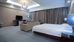 Ein modernes Hotelzimmer mit einem großen Bett, einem Flachbildfernseher, einer Sitzecke und einer Kandelaberleuchte.