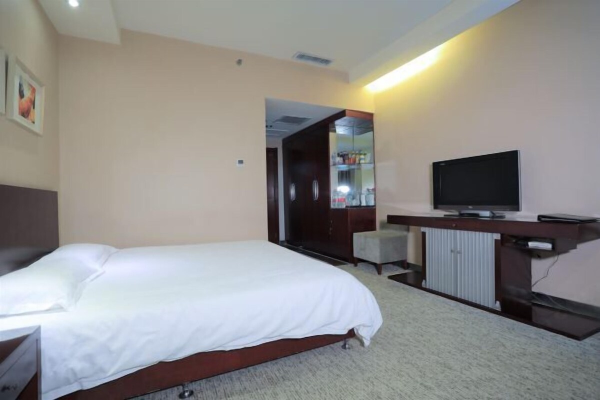 A hotel room with a bed, a desk with a television, a mirror, and a wardrobe.