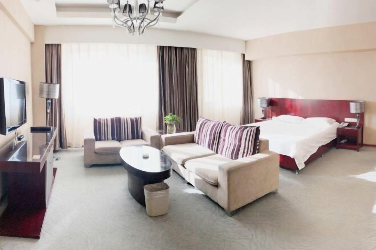 A hotel room with a bed, a sofa, a TV, a coffee table, and a desk.
