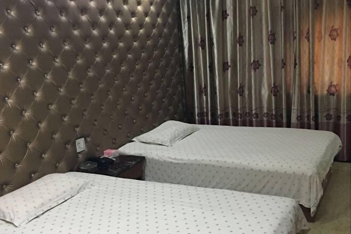 Un dormitorio con dos camas, un cabecero capitonado y una cortina con estampado floral.