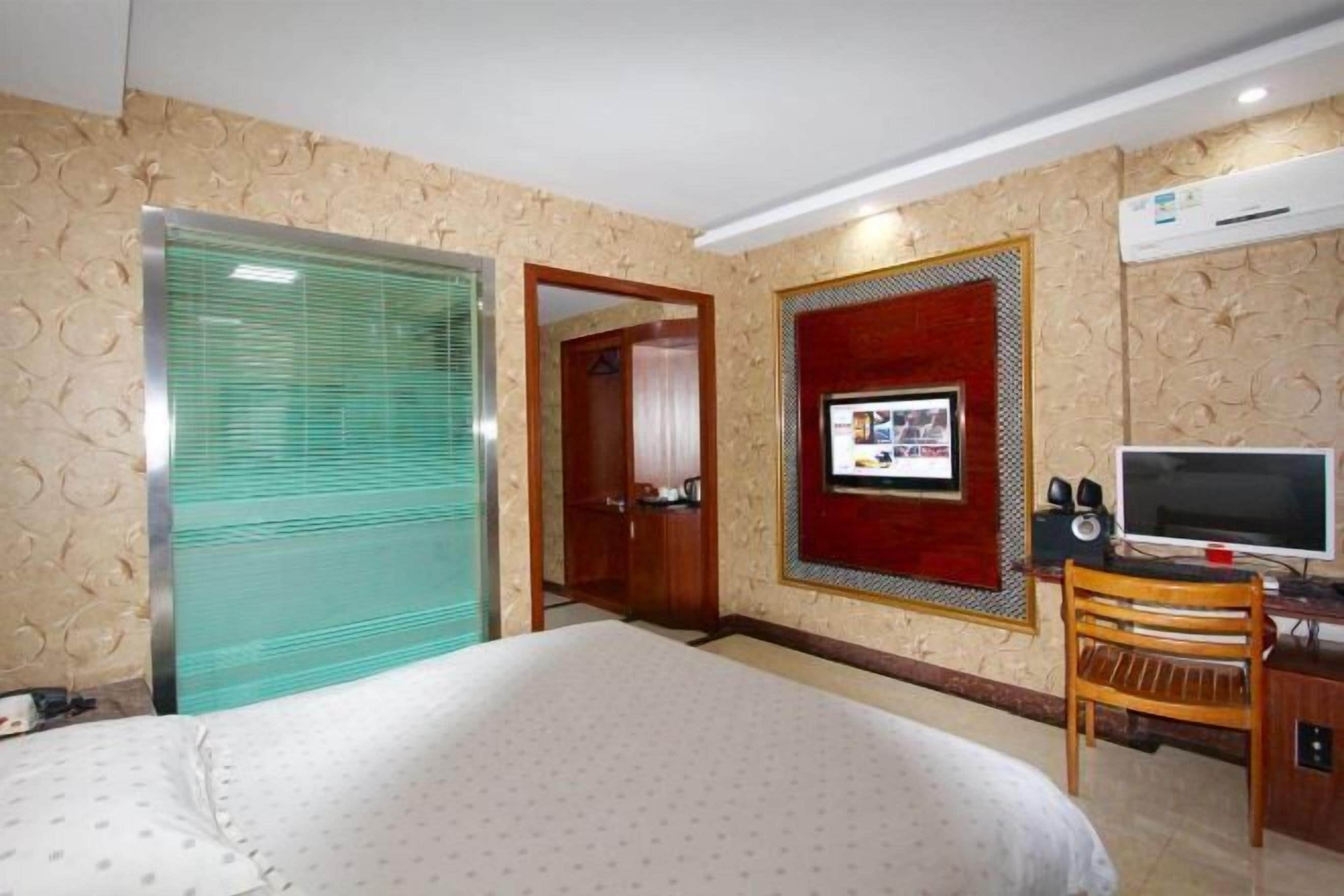 A hotel room with a bed, a television, a desk with a computer, and an air conditioning unit.