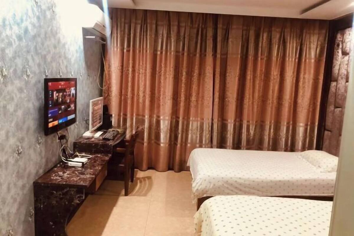 Habitación de hotel con una cama, un escritorio con computadora, televisor montado en la pared y ventana con cortinas.