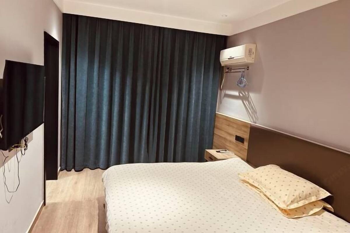 Una habitación de hotel con cama, televisión, escritorio y ventana con cortinas.