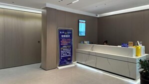 A modern reception area with a digital display, a reception desk, and a vertical information board. - Hongdu Hotel (Tongxiang)