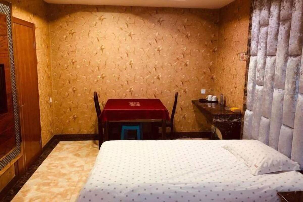 Una habitación de hotel con una cama, una mesita con mantel rojo, una silla y una mesita de noche con lámpara.