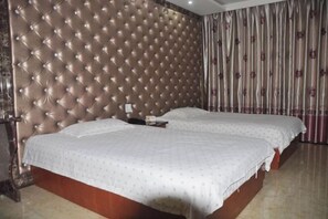 Una camera d'albergo con testiera trapuntata, due letti, un comodino e una tenda a righe.
