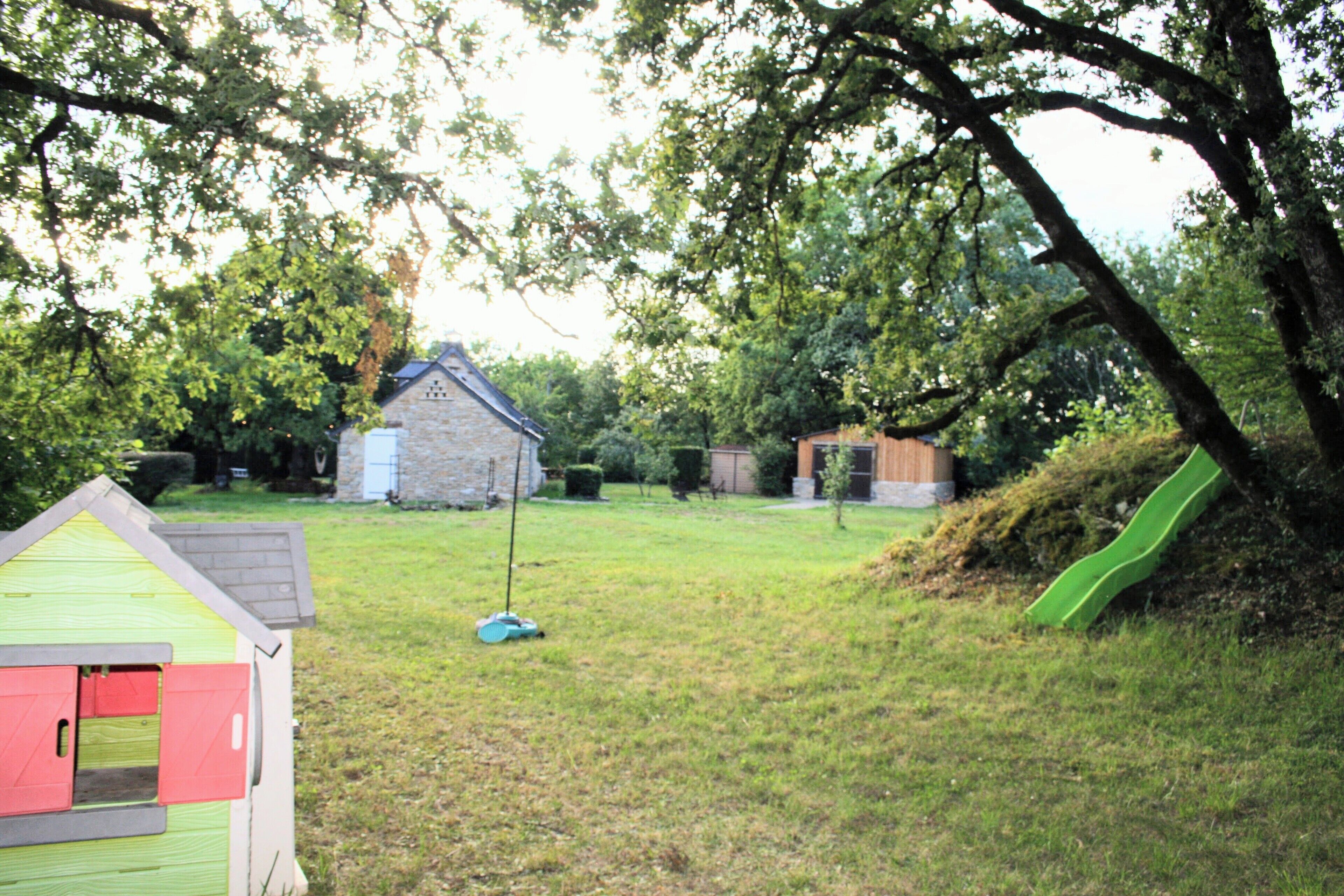 Un jardin avec une petite maison de jeu, un toboggan et un bâtiment en pierre.