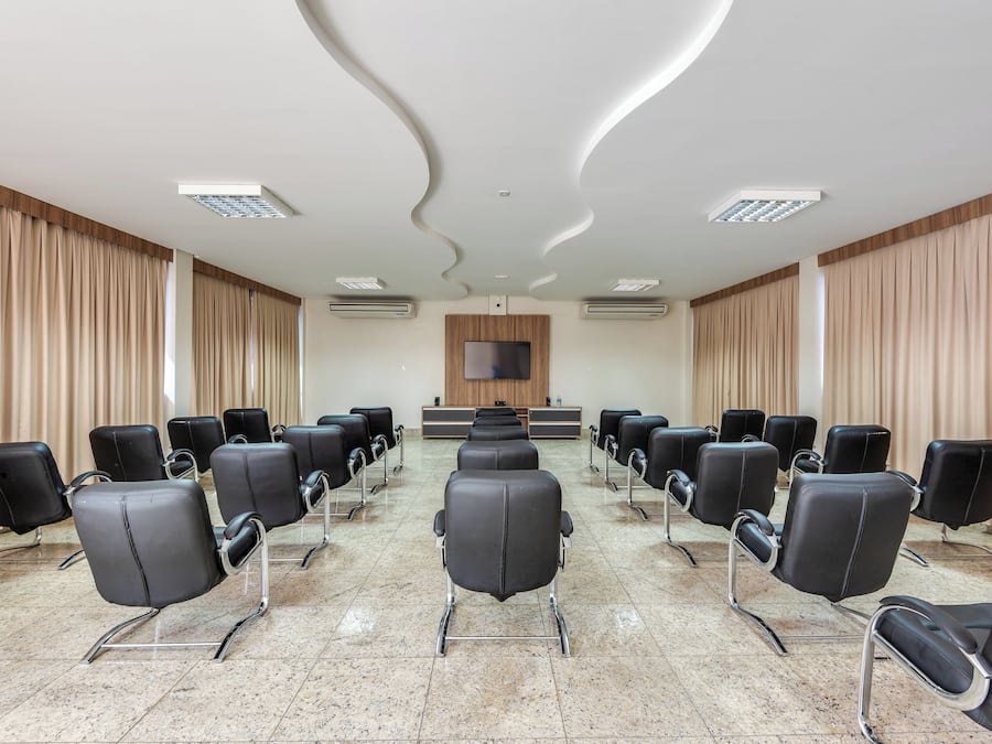 Un salón de conferencias con filas de sillas negras, un televisor de pantalla plana en la pared y un diseño de techo moderno.
