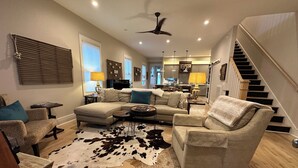 A spacious living room with a sectional sofa, a coffee table, and a cowhide rug. A staircase leads to the upper floor, and a ceiling fan is visible. - Great Location!  Charming 3-bedroom townhome in brilliant Nashville w/ AC, WiFi (Nashville)