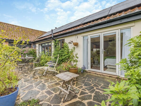 A stone patio with a table and chairs, a hanging basket, and potted plants.
