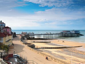 A coastal beach with a pier extending into the sea, a promenade, and buildings along the shore.