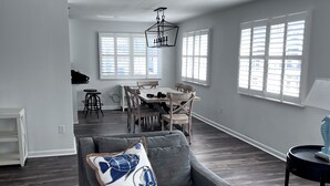 A spacious living room with a grey sofa, a wooden dining table, and a chandelier.