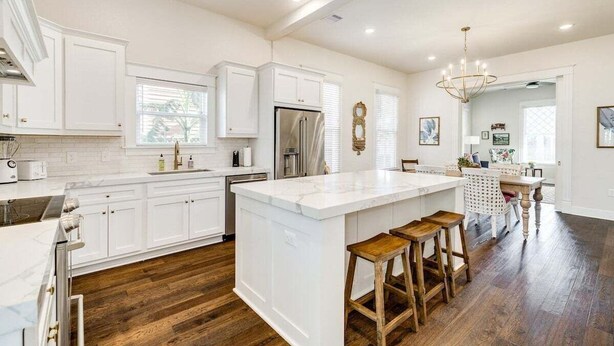 A spacious kitchen with white cabinetry, a large island with stools, and a wooden floor. - La Onda Azul (Galveston)