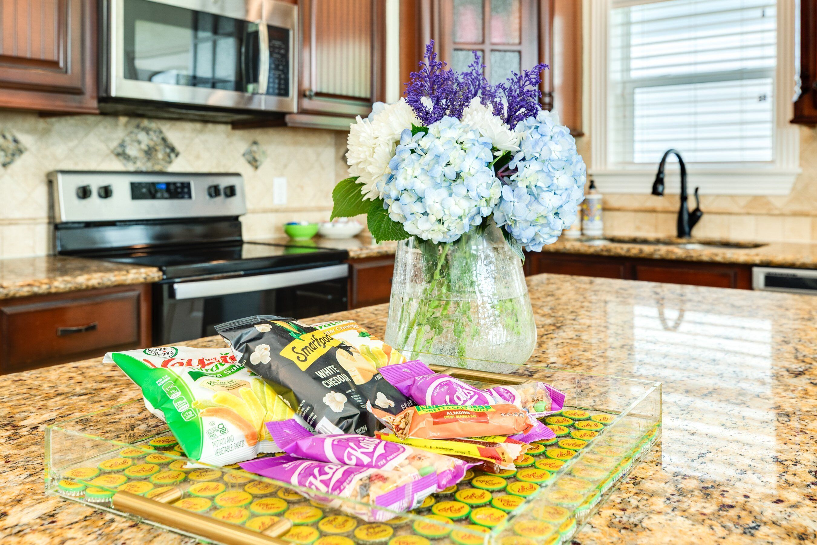 A kitchen counter with a vase of flowers, a plate of snacks, and a bag of chips.