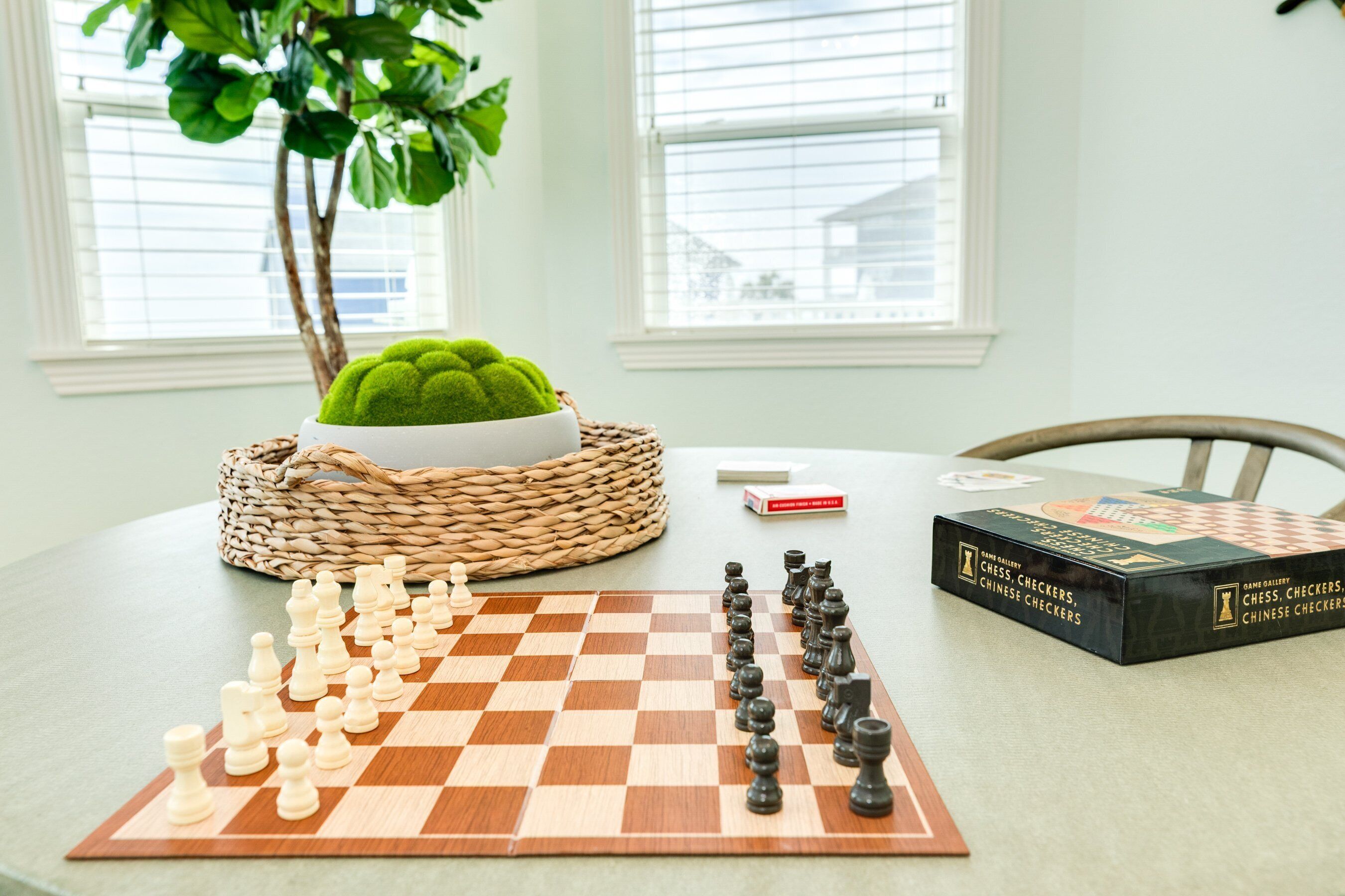A chessboard set up on a table with a chess set and a book titled "Chess, Checkers, Chinese Checkers" beside it.