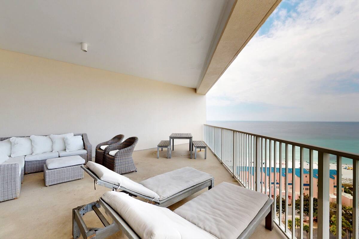 A balcony with wicker furniture, a small table, and a view of the beach.