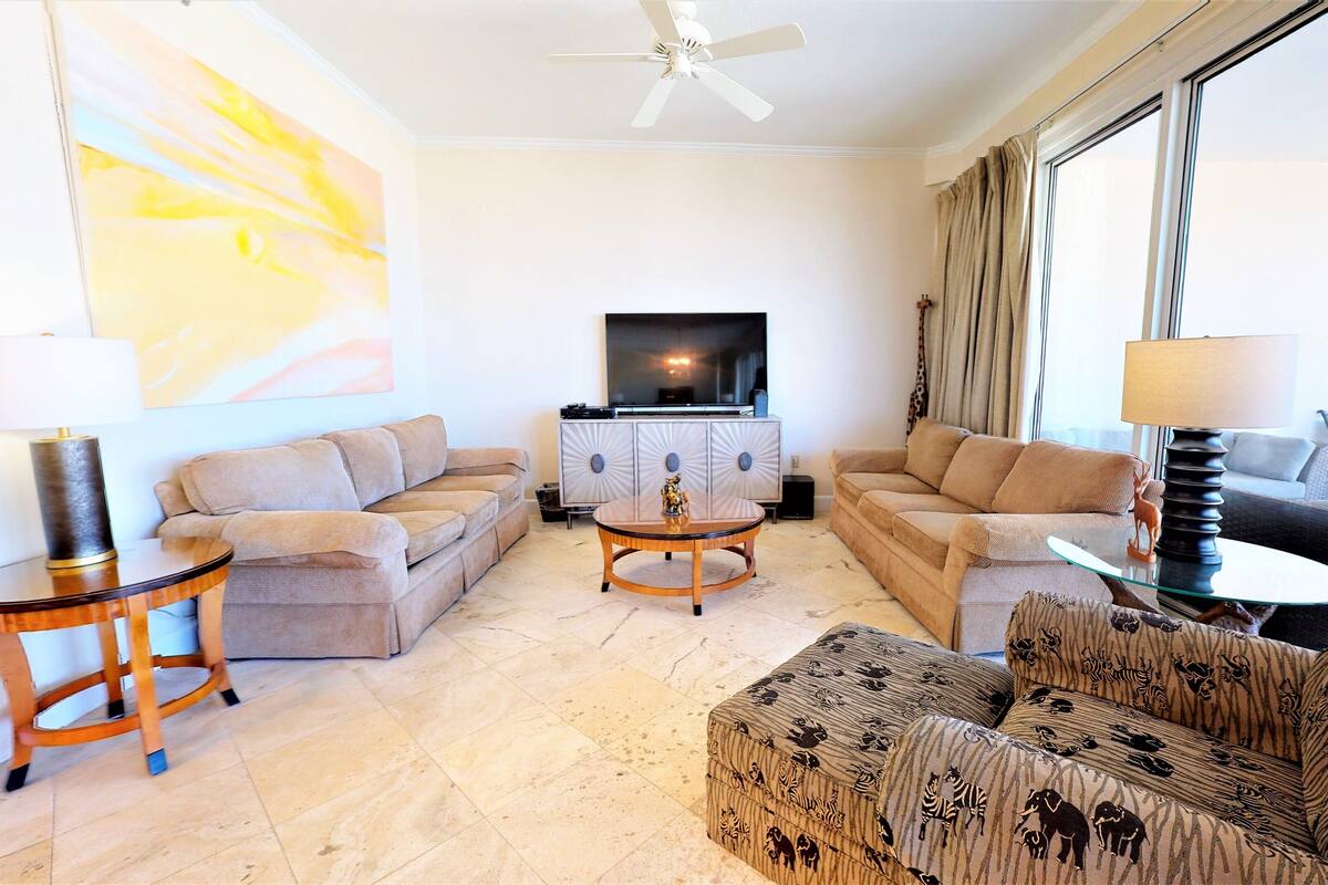 A living room with a sofa set, a coffee table, a TV, and a large window with curtains.