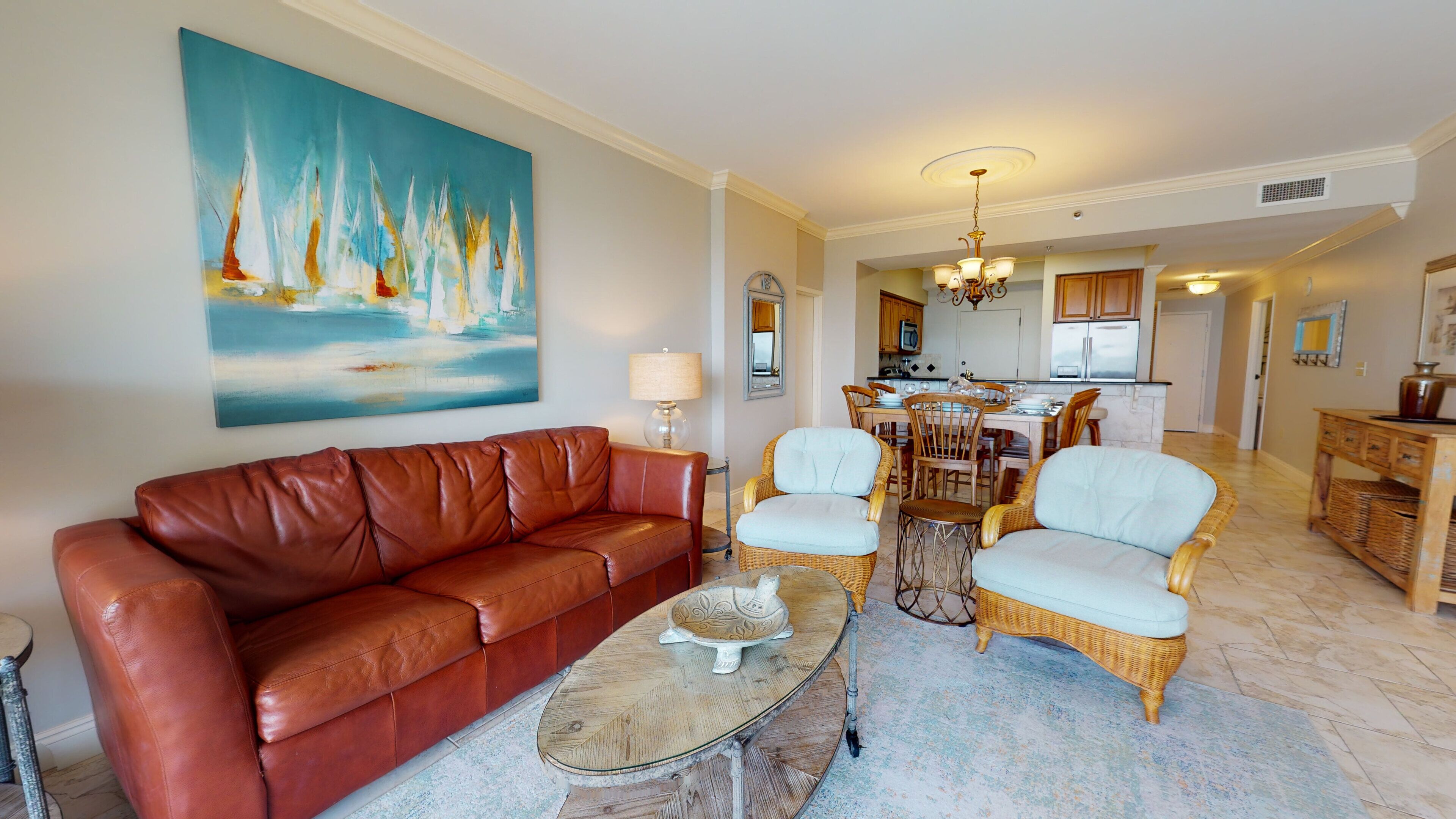 A living room with a brown leather sofa, two wicker chairs, a coffee table, and a painting of sailboats.