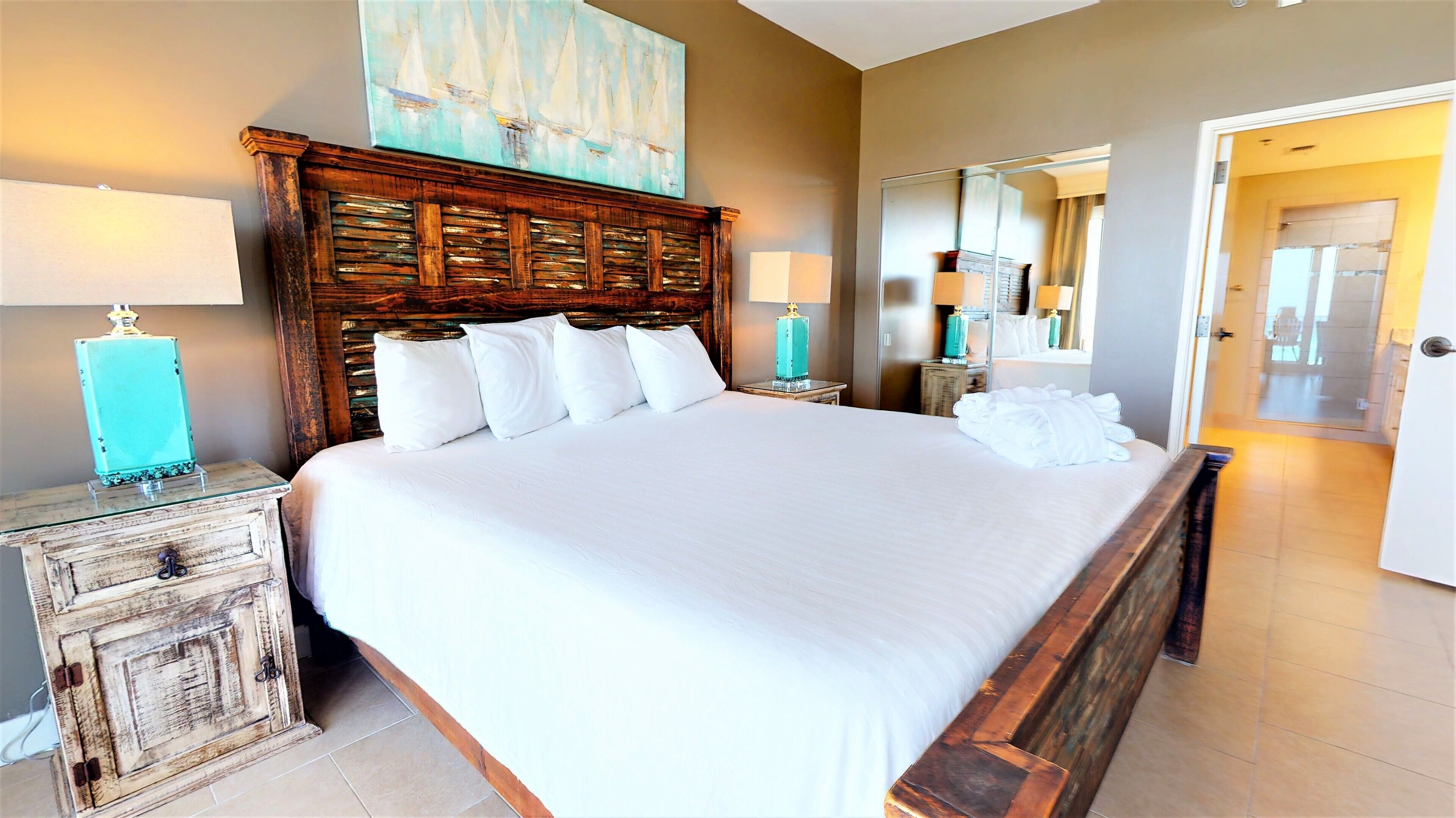 A large bed with a wooden headboard, two bedside tables with lamps, and a painting above the headboard.