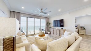 Un soggiorno spazioso con una grande TV a schermo piatto, una ventola a soffitto e un balcone con vista sull'oceano.