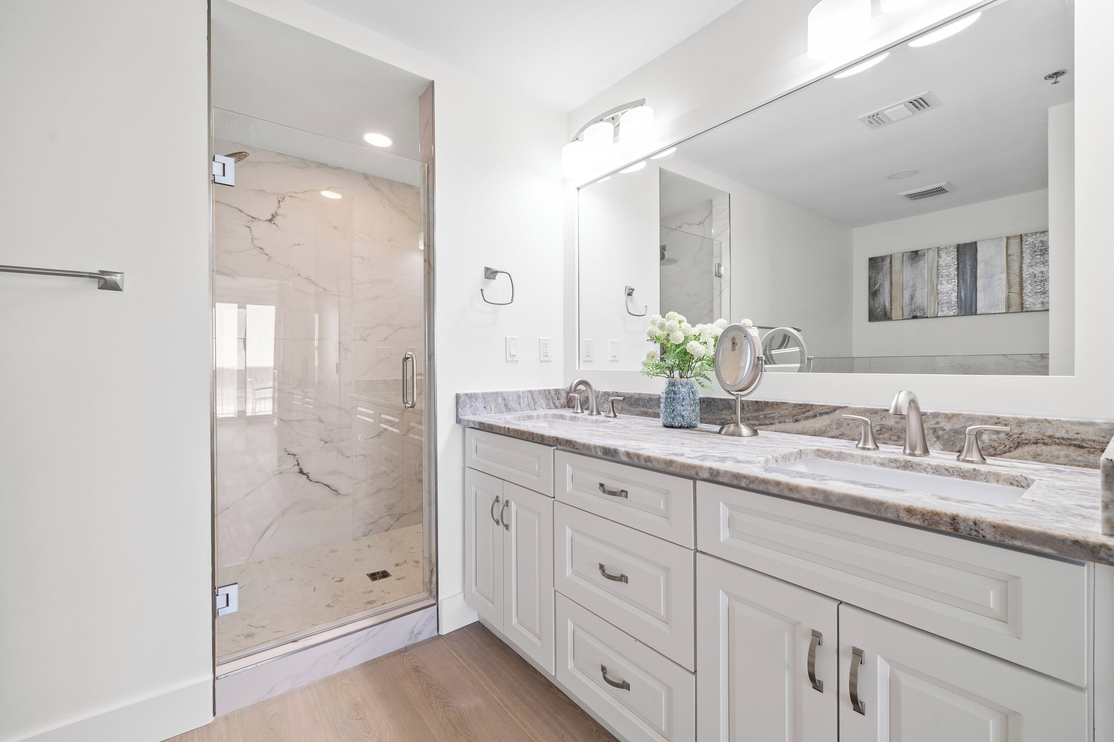 A modern bathroom with a glass shower enclosure, a large vanity with a marble countertop, and a wall-mounted mirror.