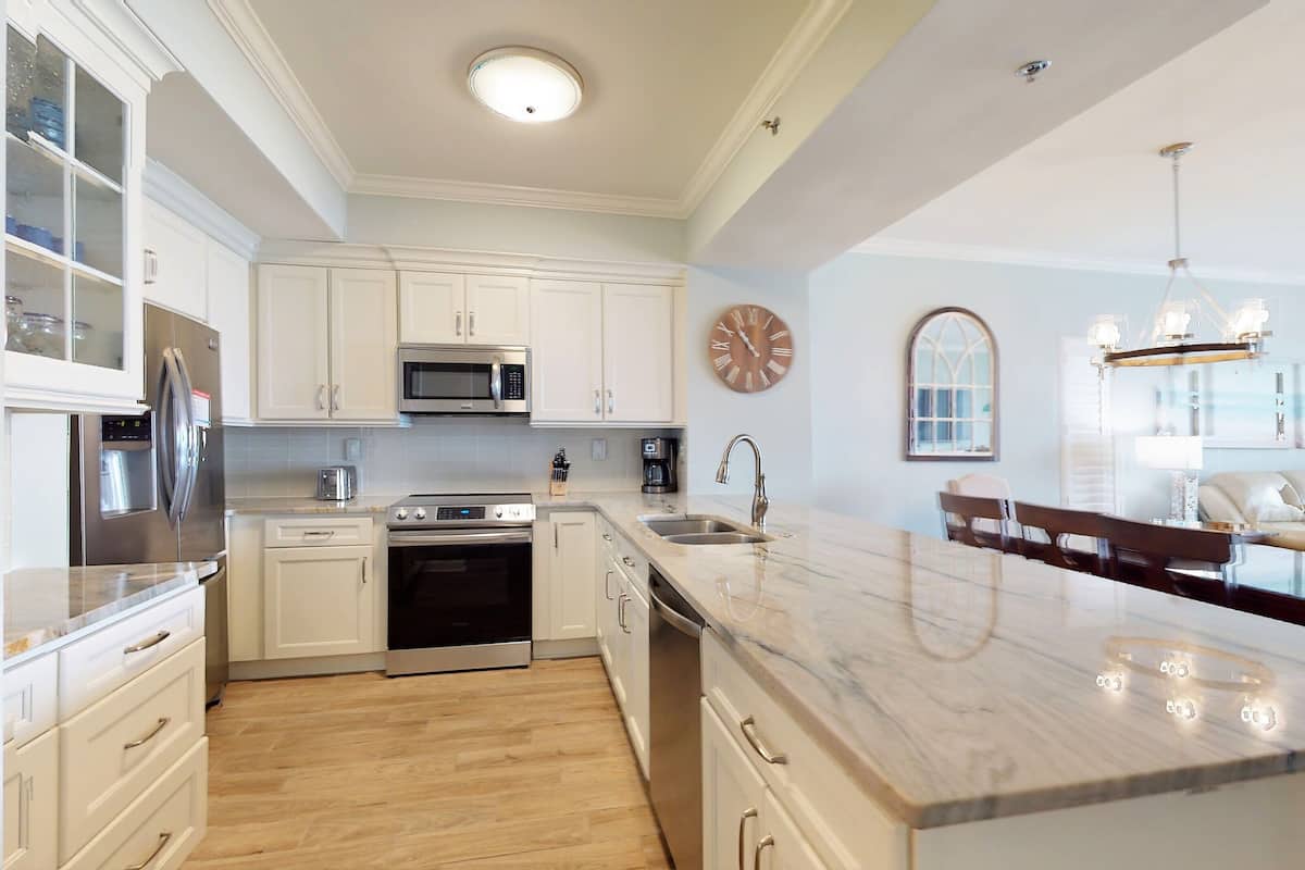 A modern kitchen with white cabinetry, stainless steel appliances, a marble countertop, and a large island.