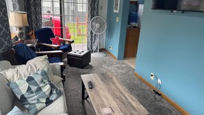 Ein Wohnzimmer mit einer Couch, einem Couchtisch, einem Ventilator und einem Fernseher.
