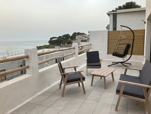 A terrace with wooden furniture, a hanging chair, and a view of the sea.