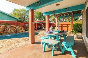 A covered patio area with a pool, stone-tiled floor, and a wooden fence. - Tortuga Inn (Galveston)