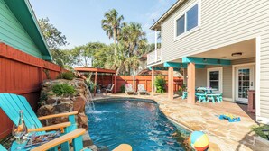 En baghave med swimmingpool, stenbelagt terrasse og udendørs siddeområde.