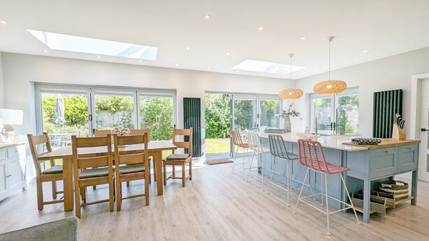 A modern kitchen with wooden furniture, a central island, and a view of the garden through large windows. - A family house that sleeps 6 guests  in 3 bedrooms (West Wittering)