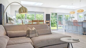 A modern living room with a large sectional sofa, a round coffee table, and a dining area with bar stools. - A family house that sleeps 6 guests  in 3 bedrooms (West Wittering)