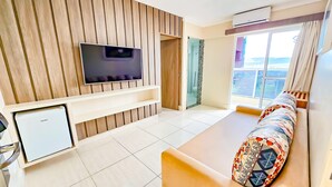 A modern living room with a flat-screen TV, a mini-fridge, a sofa with patterned cushions, and a sliding glass door leading to a balcony. - DiRoma Piazza - Direto com o Grupo DiRoma - acesso ao Acqua Park com café da manhã (Caldas Novas)