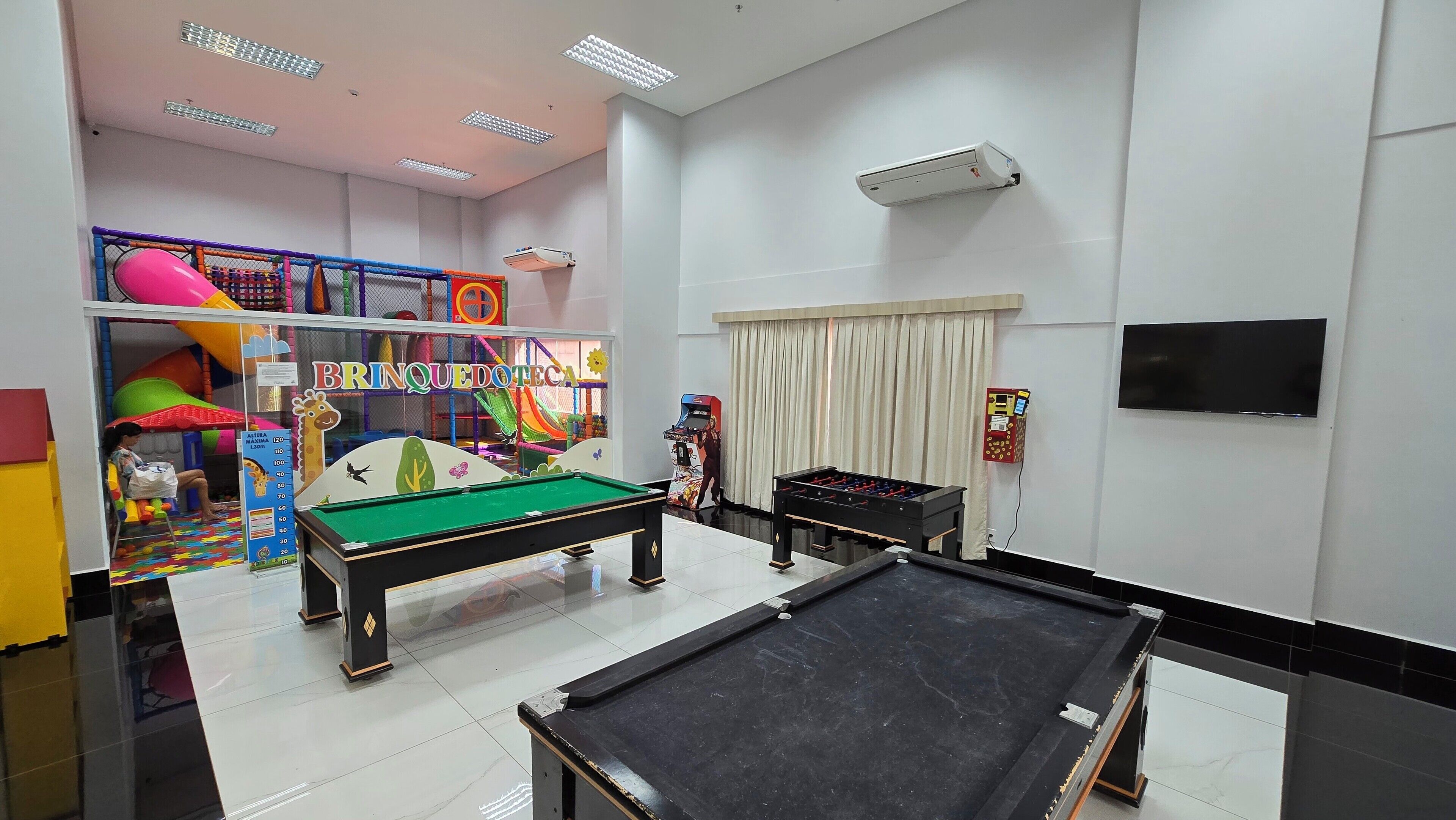 A recreational room with a pool table, foosball table, and a children's play area with colorful equipment.