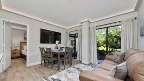 A modern living room with a brown leather sofa, a dining area with wooden chairs and a table, and a large window with curtains. - Luxury 2 Suites, Near Parks and Int'l Drive (Orlando)