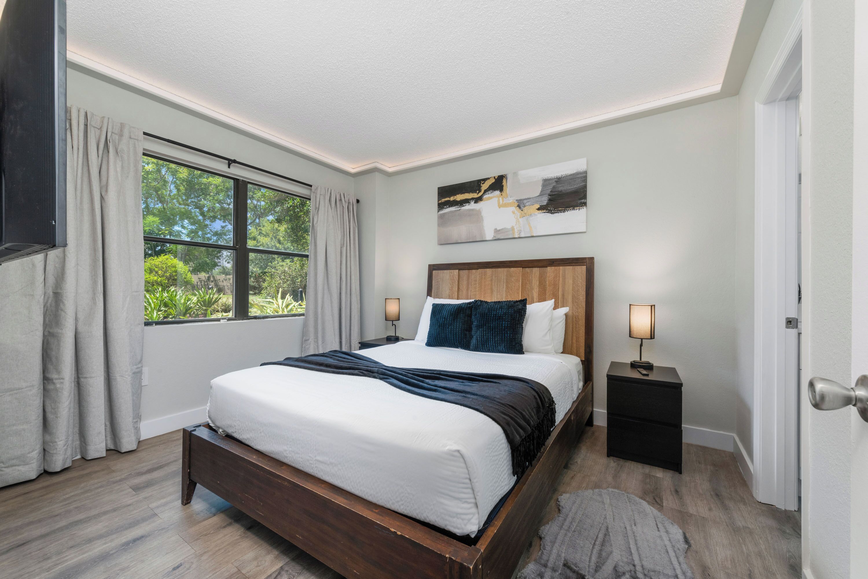 Une chambre avec un grand lit, une table de chevet, une œuvre d’art accrochée au mur et une fenêtre avec des rideaux.