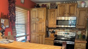 A kitchen with wooden cabinets, a microwave, an oven, and a bar area with stools. - Cozy 3 bedroom with loft,  condo in welcoming Angel Fire with WiFi (Angel Fire)