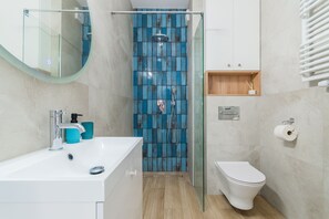 A modern bathroom with a glass shower enclosure, a white sink, and a toilet. - Doki - Curacao by Grand Apartments (Gdansk)