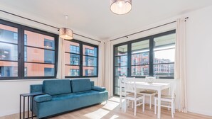 En moderne stue med en blå sofa, et spisebord med stole, store vinduer og en hængende lampe.