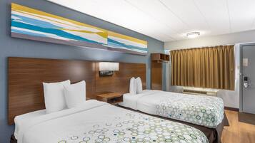 A hotel room with two beds, a nightstand, a wall-mounted lamp, a window with curtains, and a door.