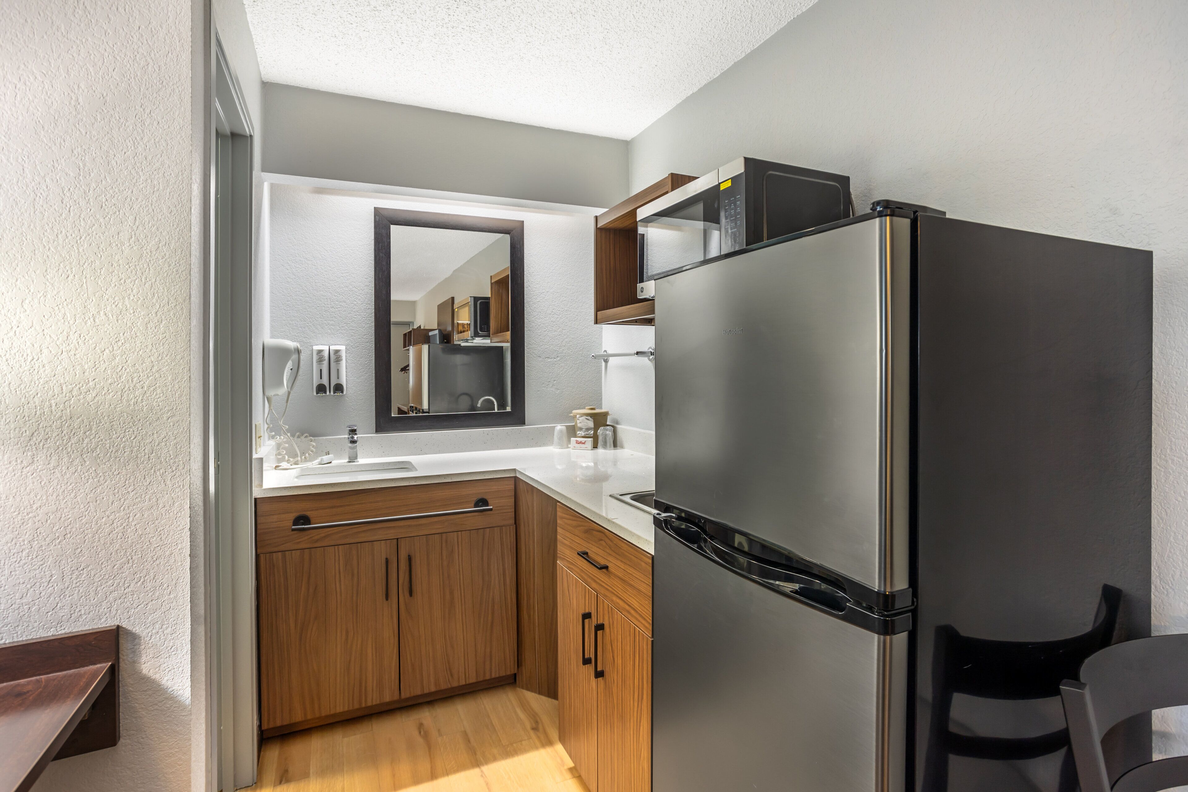 A compact kitchen with a built-in refrigerator, wooden cabinets, a countertop, and a mirror above the sink.