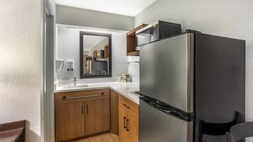 A compact kitchen with a built-in refrigerator, wooden cabinets, a countertop, and a mirror above the sink.
