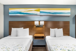 Una habitación de hotel con dos camas, cabecero de madera, mesita de noche y lámpara fijada a la pared.