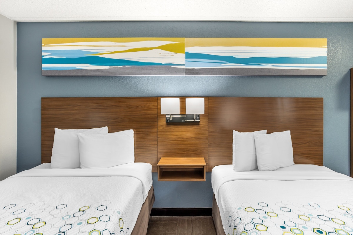 Une chambre d’hôtel avec deux lits, une tête de lit en bois, une petite table de chevet et un luminaire fixé au mur.