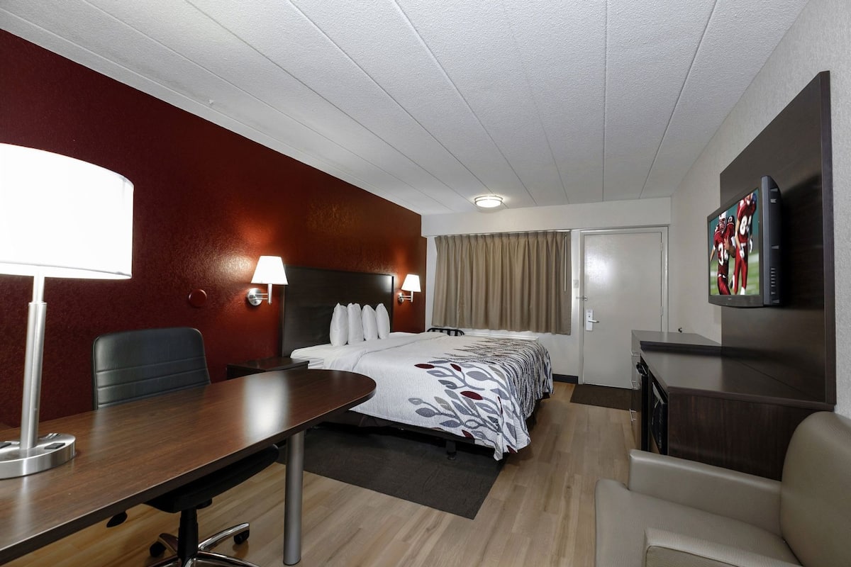 Una habitación de hotel con cama, escritorio, silla, televisión y ventana con cortinas.
