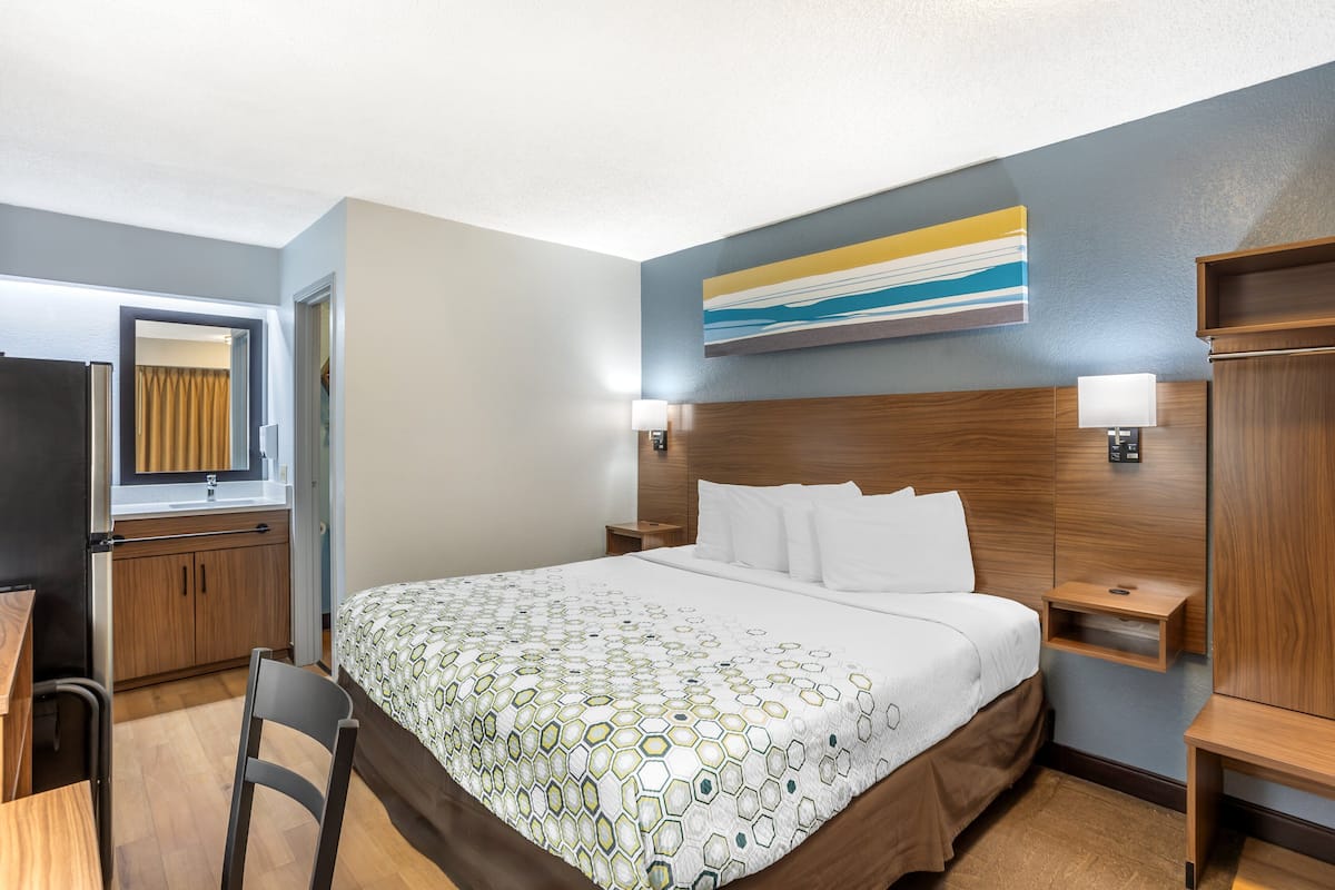 Habitación de hotel con cama, escritorio, silla, mesita de noche y estante fijado a la pared.