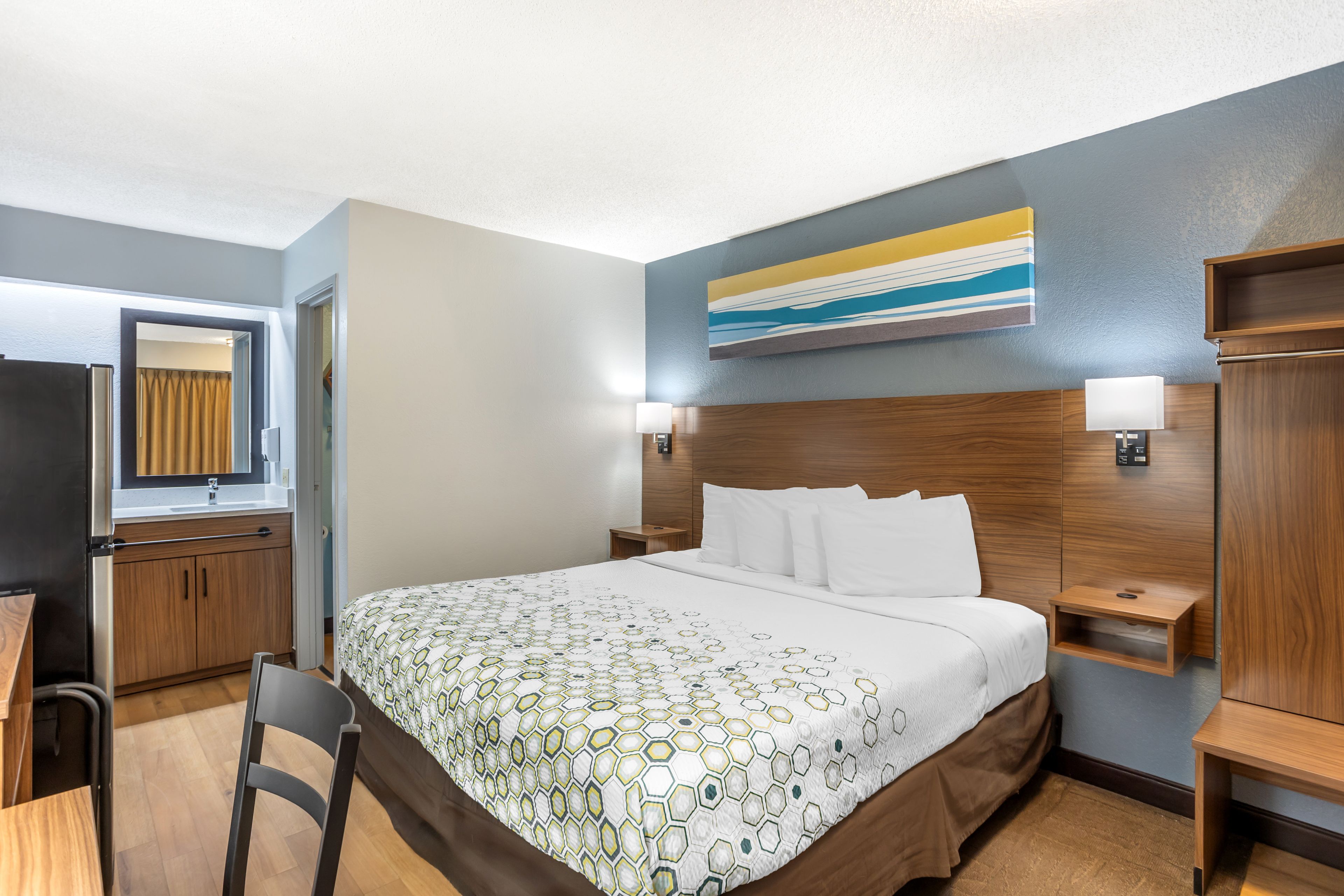 Een hotelkamer met een bed, bureau, stoel, kledingkast en een schilderij aan de muur.