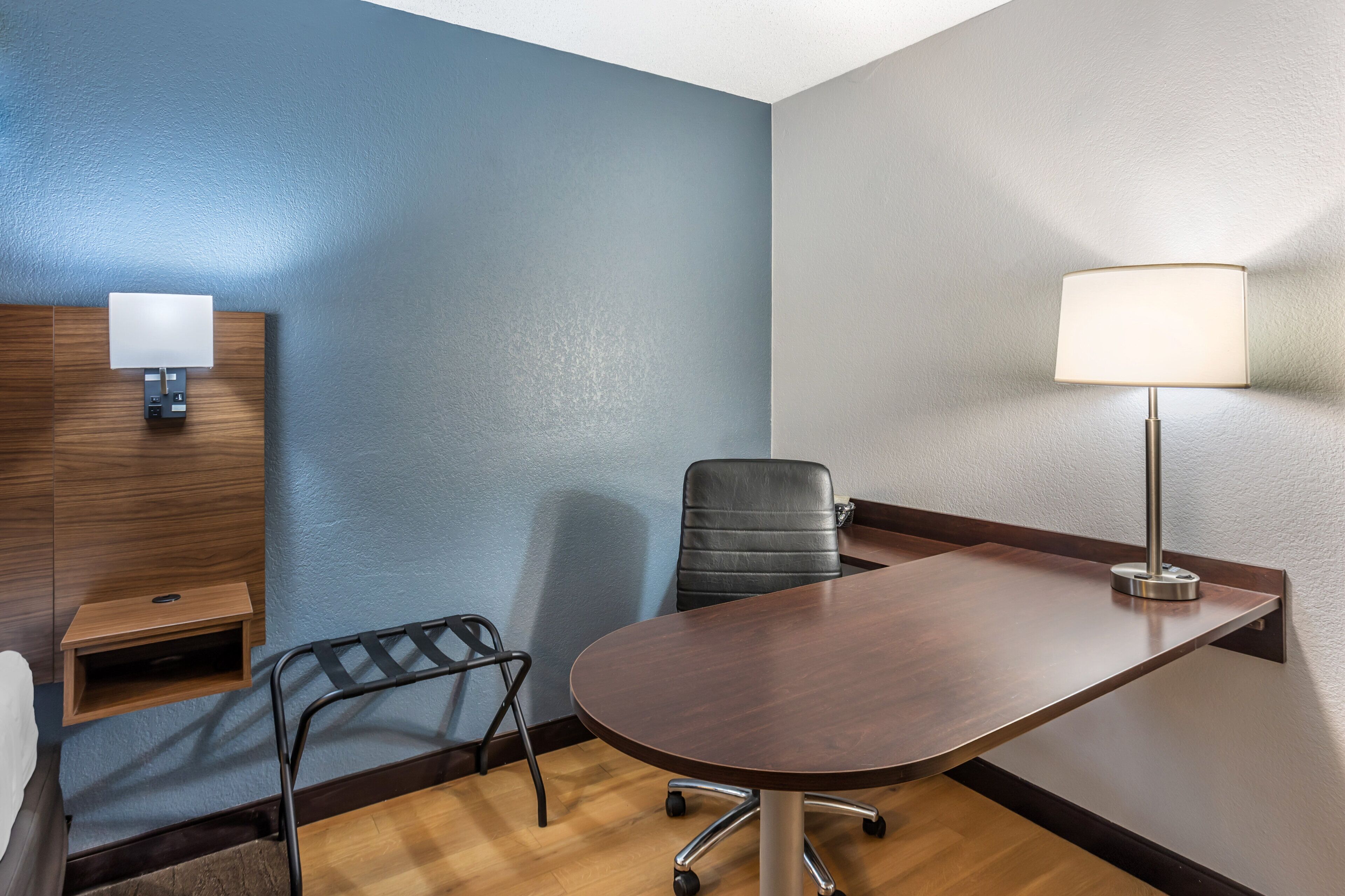Une salle de conférence avec une table en bois, un fauteuil de bureau noir, une lampe de bureau et un luminaire fixé au mur.
