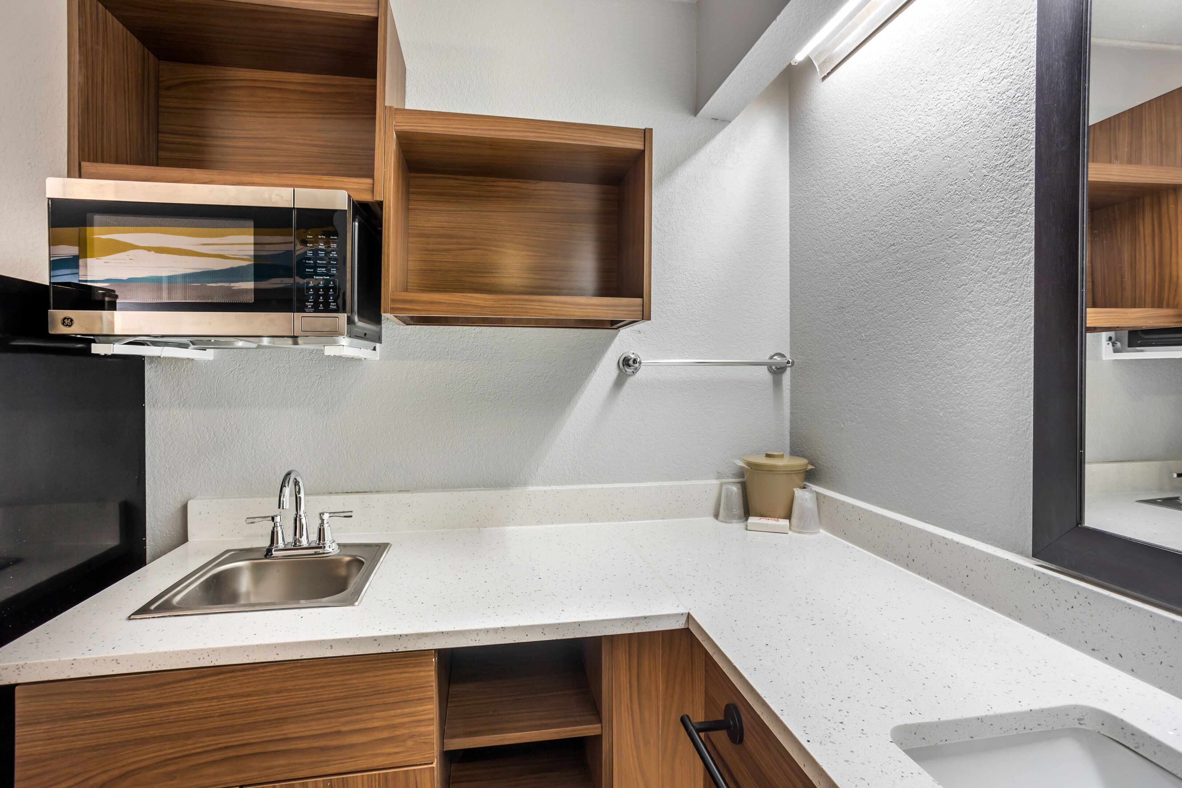 A kitchen with a built-in microwave, stainless steel sink, wooden cabinets, and a white speckled countertop.